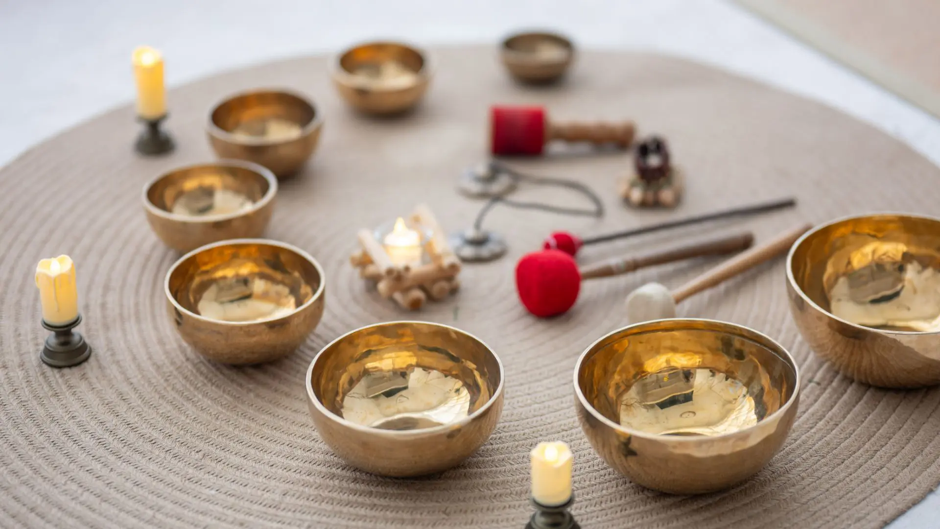 3.GettyImages-2182414352 Several golden singing bowls with mallets arranged on a white surface.
