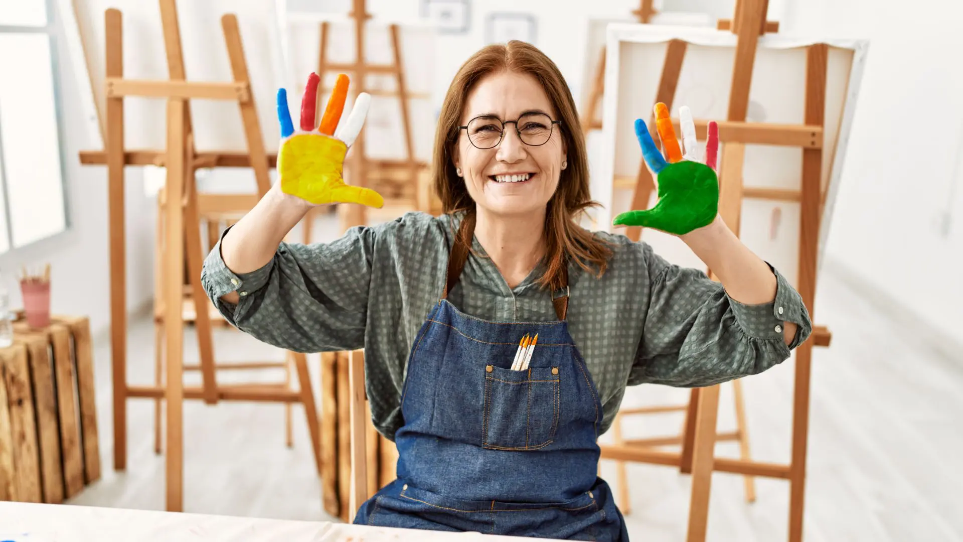 4.GettyImages-1327849351 Smiling woman holding colorful handprints in an art studio.