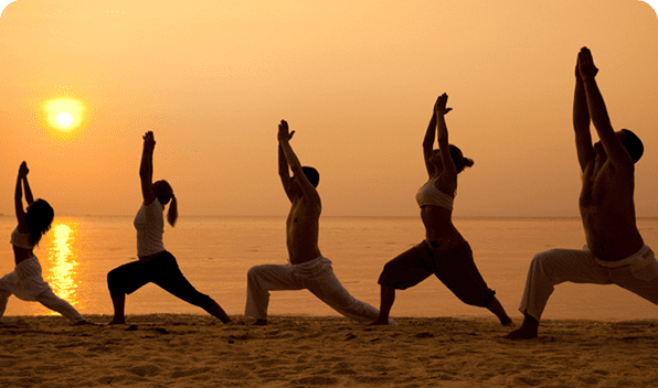 Three people practicing yoga on the beach at sunset.