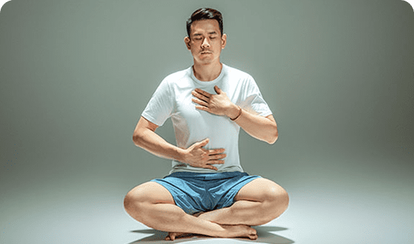 A man sitting cross-legged, meditating with eyes closed and hands on chest and stomach.