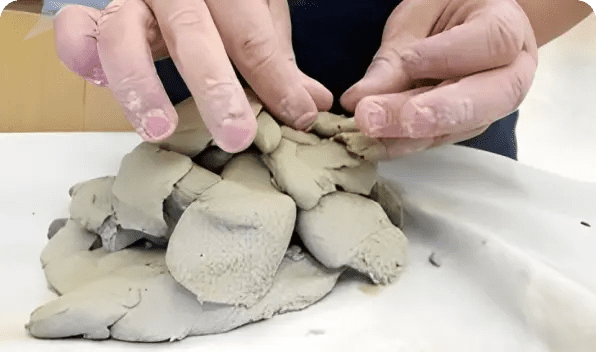 Hands shaping soft clay into small figures on a flat surface.