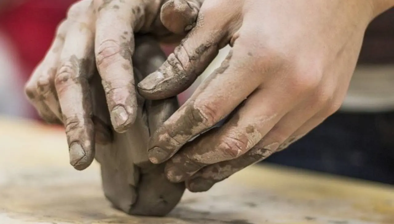 Two hands shaping clay in a pottery process.
