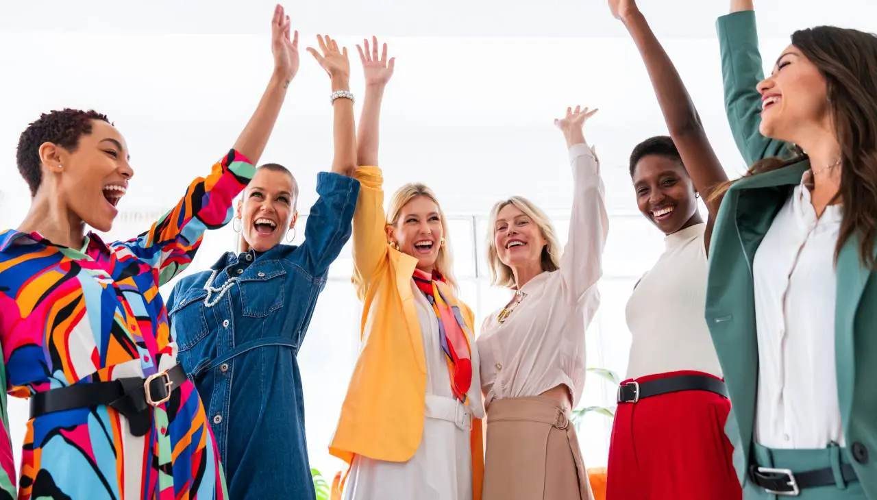 A group of four joyful women raising their hands.