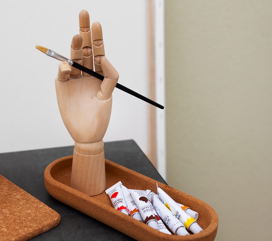 woman-outdoors-holding-singing-bowl 2 A wooden hand model holding a paintbrush above a tray with paint tubes.
