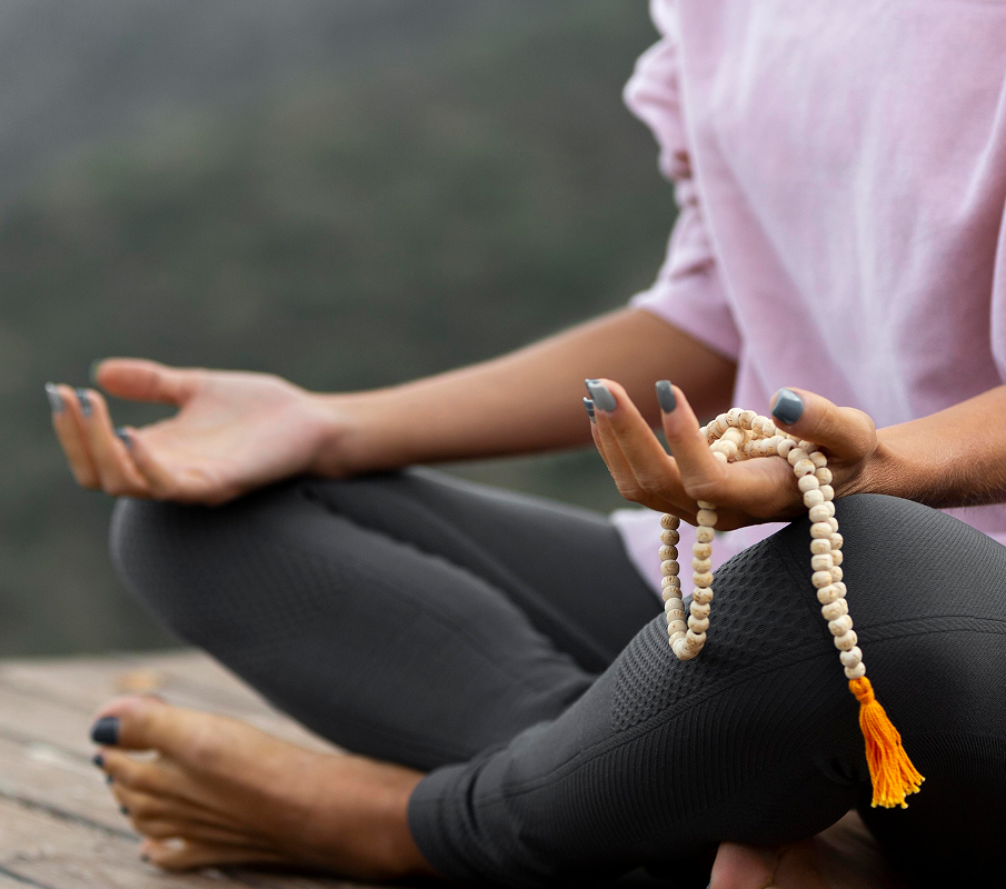 woman-outdoors-holding-singing-bowl 2 (1) Person meditating outdoors with prayer beads in hand.