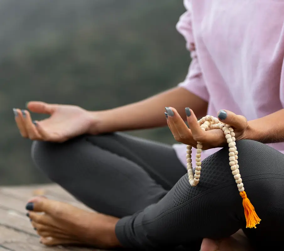 Person meditating outdoors holding mala beads