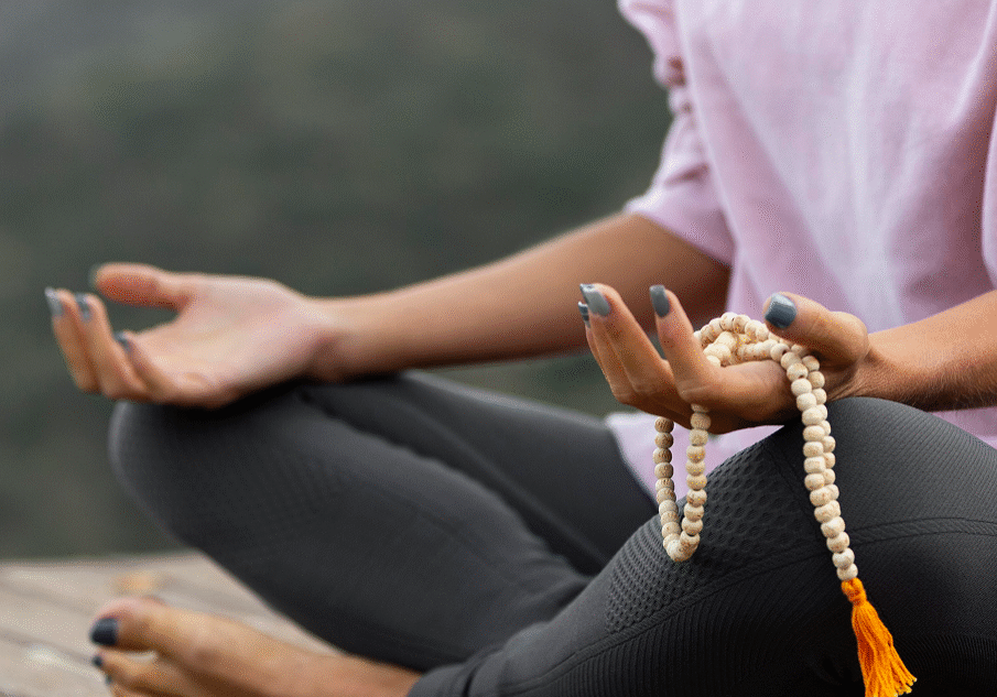 Person meditating outdoors with prayer beads in hand.