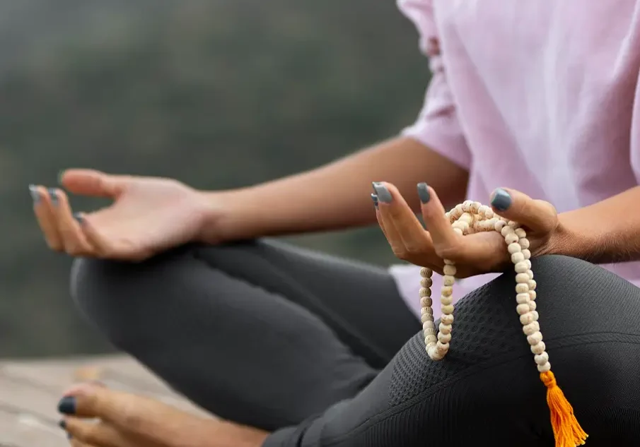 Person meditating outdoors holding mala beads